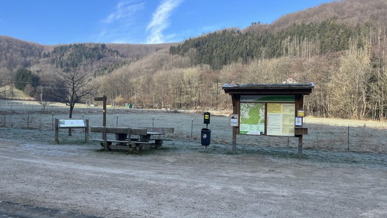 Een rustige plek met een informatiepunt en een bank in de natuur. Op de achtergrond zijn zachte heuvels en een blauwe lucht te zien.