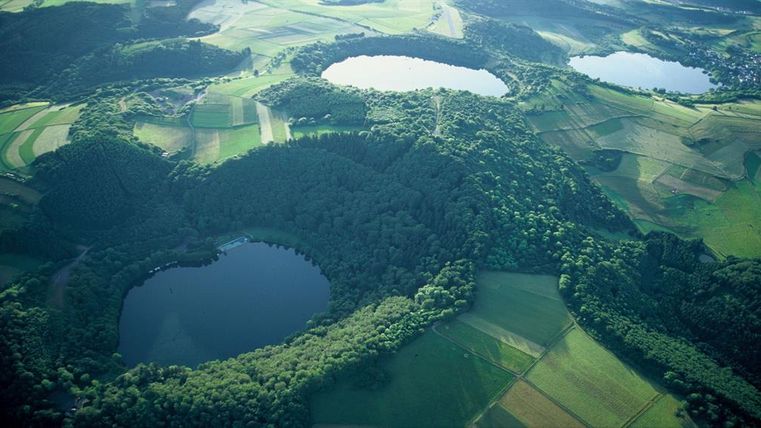 Eine Luftaufnahme von mehreren Seen, umgeben von grünen Wäldern und Feldern. Die Landschaft ist friedlich und einladend, mit sanften Hügeln in der Umgebung.
