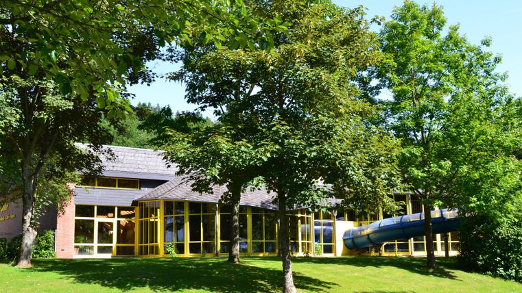 Ein modernes Gebäude umgeben von Bäumen und Rasen. Zu sehen ist auch eine Rutsche in der Nähe des Eingangs.