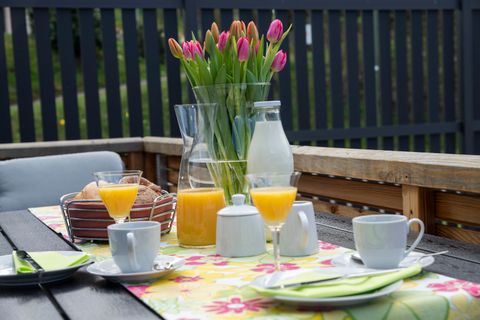 A set table outdoors with fresh tulips and various drinks. There is orange juice, milk, and small snacks on a colorful tablecloth.