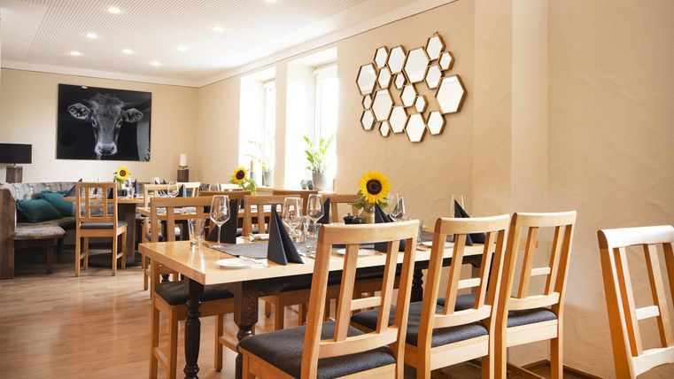 Een modern restaurant met houten tafels en stoelen. De muren zijn licht geverfd en versierd met een kunstwerk en spiegels.