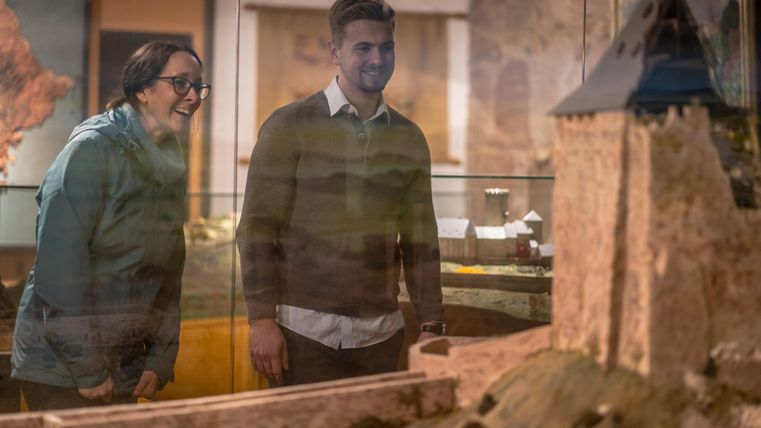 Two visitors are looking at a model of a castle in a museum with interest. The two seem excited about the exhibition.
