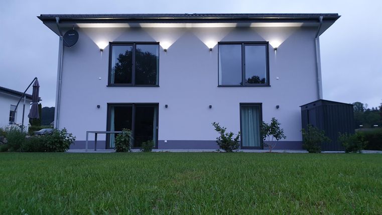 Ein modernes Haus mit hellen Fenstern und einem gepflegten Garten. Die Fassade ist schlicht und elegant, umgeben von grüner Rasenfläche.