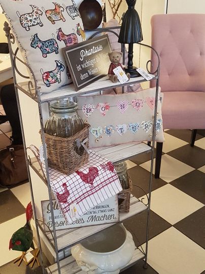 Ein eleganter Regalständer mit verschiedenen Dekorationsartikeln und Küchenaccessoires. Darunter befinden sich Stoffe, Körbe und ein Kissen mit bunten Mustern.