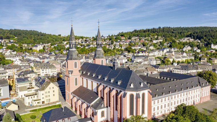 Eine beeindruckende Kirche mit zwei hohen Türmen steht im Mittelpunkt der Stadtansicht. Umgeben von grünen Hügeln und einem malerischen Stadthorizont.