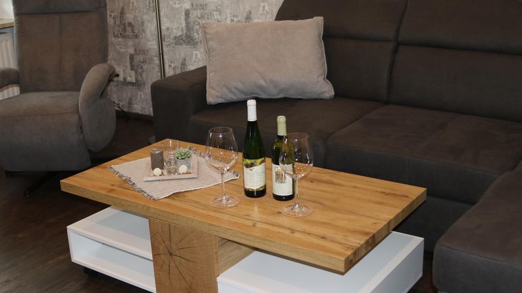 Ein gemütliches Wohnzimmer mit einem modernen, braunen Sofa und einem stilvollen Holztisch. Auf dem Tisch stehen zwei Weine und Gläser.