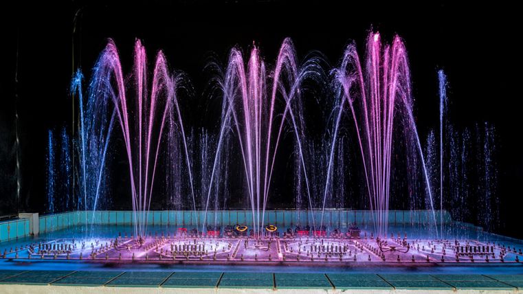 Illuminated water features in a rectangular pool with many colorful water jets.