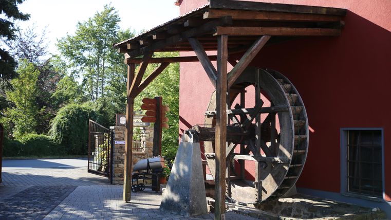 Ein historisches aber gut erhaltenes Wassermühlrad an einer roten Hausfassade.