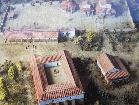 A model of an ancient settlement with several buildings and red roofs. The surroundings are designed with trees and plants.