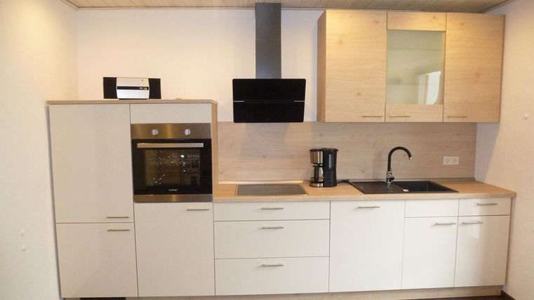 Eine moderne Küche mit weißen Schränken und einem Essbereich. Sie ist ausgestattet mit einem Herd, einem Wasserhahn und einem Kühlschrank.