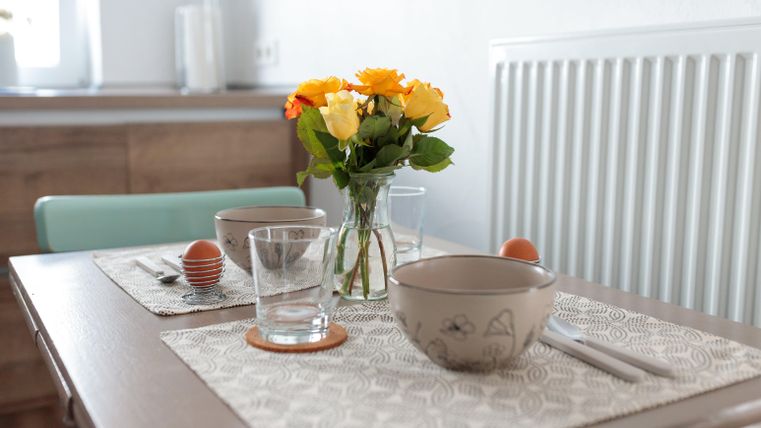 Ein hübsch gedeckter Tisch mit zwei Schalen, Gläsern und Eiern. In der Mitte steht ein Blumenstrauß aus gelben und orangefarbenen Rosen.
