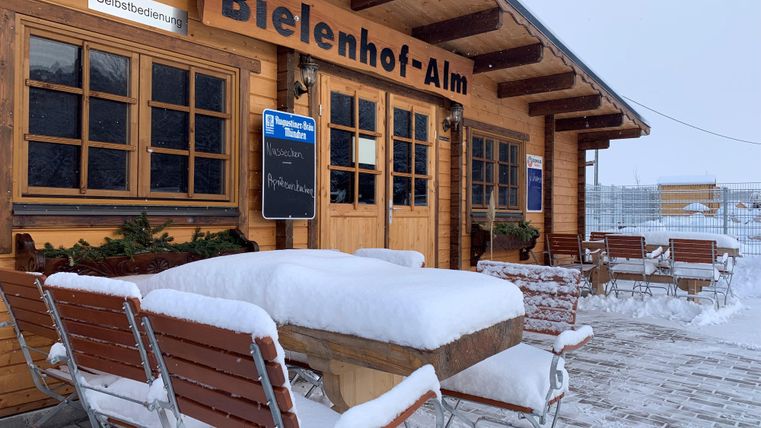 Een besneeuwde berghut met houten tafels en stoelen buiten.