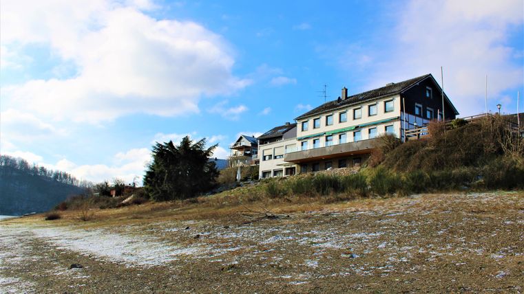 Een huis op de heuvel met uitzicht op een heldere lucht en enkele wolken. De grond is droog en heeft een natuurlijke omgeving.