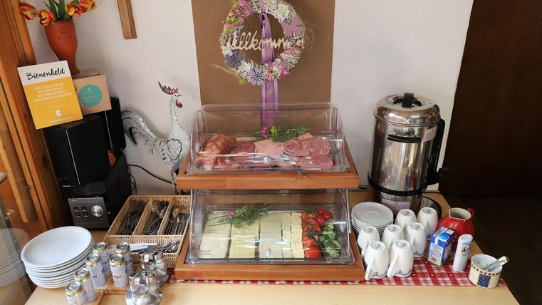 A buffet with different types of meat, fresh vegetables, and cheese. There are also coffee pots and dishware on a table.