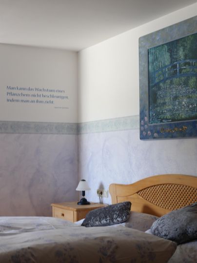 Ein gemütliches Schlafzimmer mit einem Holzbett und dekorativen Kissen. An der Wand hängt ein großes Bild und es gibt eine Nachttischlampe.