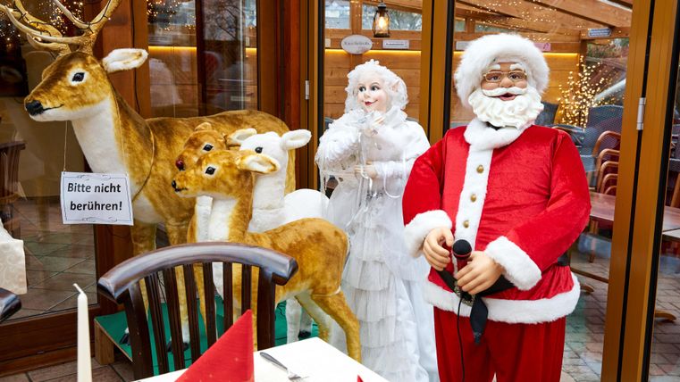 Eine festliche Weihnachtsdekoration mit einem Weihnachtsmann, einer Schneekönigin und zwei Rentiere. Der Tisch ist gedeckt mit roten Servietten.