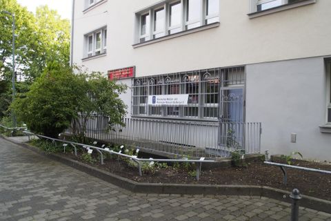 Ein Gebäude mit einem Fenster, das von einem Gitter umgeben ist. Im Vordergrund sind Pflanzen und ein gepflasterter Weg zu sehen.