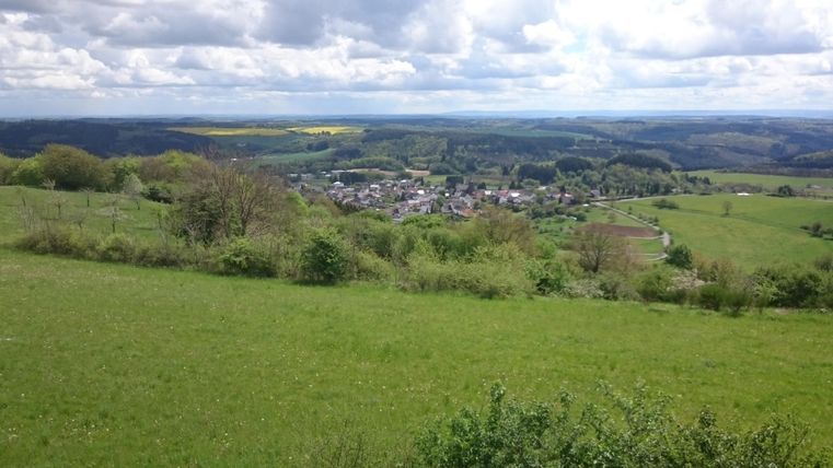 A picturesque view of a small village in the valley, surrounded by green meadows and hills. The sky is cloudy and the landscape appears soothing.