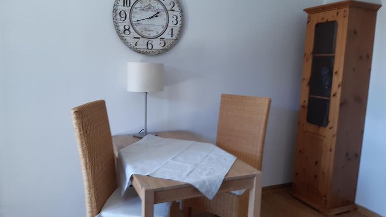 Een gezellige eetruimte met een ronde tafel, twee stoelen en een vloerlamp. Aan de wand hangt een grote klok en een houten kast staat naast de tafel.