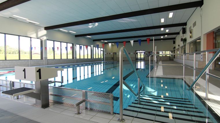 Een modern binnenzwembad met helder water en grote ramen. De trap leidt naar het zwembad, dat goed verlicht is.