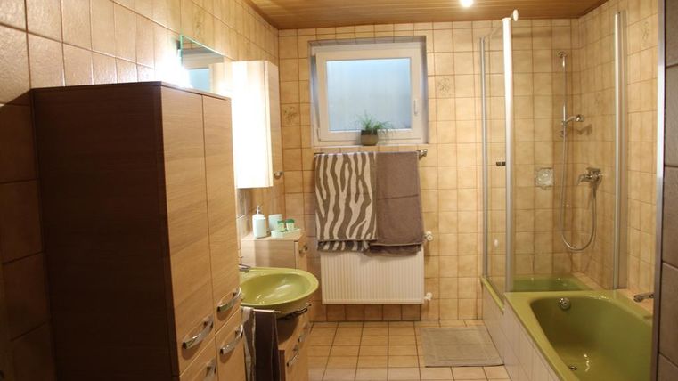 A modern bathroom with a shower and a bathtub. The walls are tiled, and there are wooden elements as well as a large mirror.