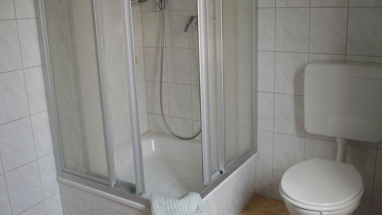 Ein einfaches Badezimmer mit einer Dusche und einer Toilette. Die Wände sind mit weißen Fliesen verkleidet.