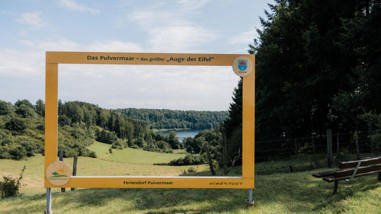 Ein schöner Ausblick auf die Landschaft mit einem großen, gelben Bilderrahmen. Im Hintergrund sind Bäume und ein Gewässer sichtbar.