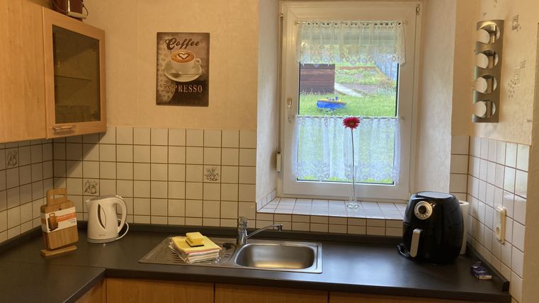 Een lichte keuken met houten kasten en een groot raam. Op het aanrecht staan een koffiepot en enkele kookgerei.