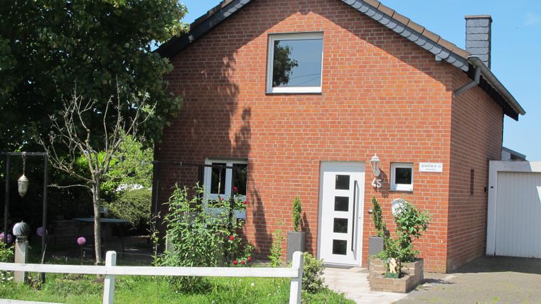 Ein rotes Backsteinhaus mit einem modernen Eingang und einem großen Fenster. Umgeben von Pflanzen und einem weißen Zaun in einer ruhigen Umgebung.
