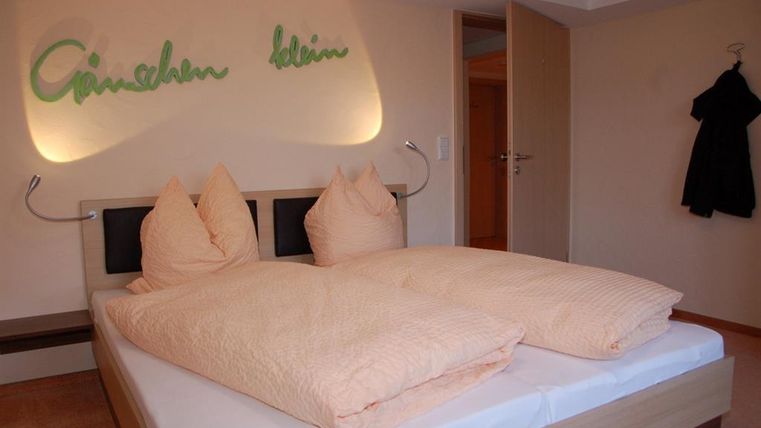 Ein gemütliches Schlafzimmer mit einem großen Bett und zwei Kopfkissen. An der Wand steht "Cinschen klein", was eine einladende Atmosphäre schafft.