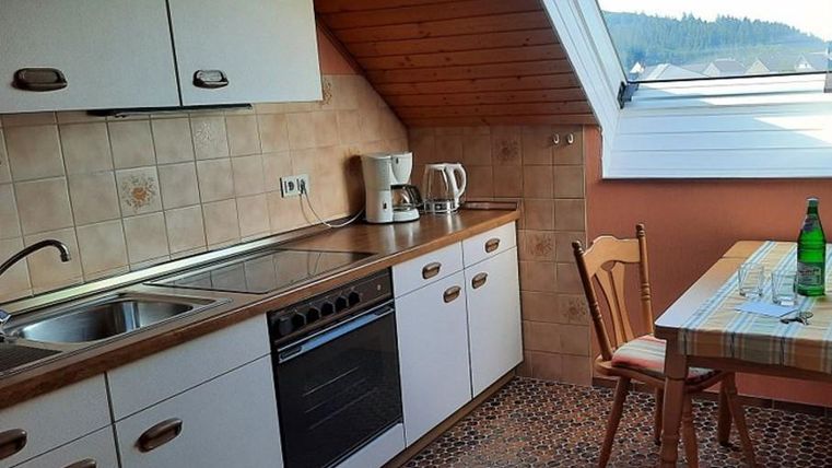 A cozy kitchenette with a modern stove and sink. A table with chairs is in the corner, surrounded by window light.