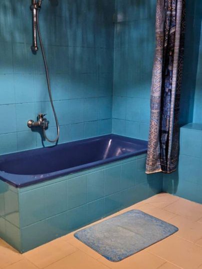 A modern bathroom with a blue bathtub and a shower. The walls are painted in a bold shade of blue, and a rug lies on the floor.