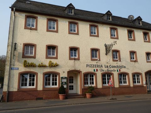 Ein gemütliches Restaurant mit der Aufschrift "PIZZERIA La Conchiglia". Die Fassade ist hell gestrichen und hat große Fenster.