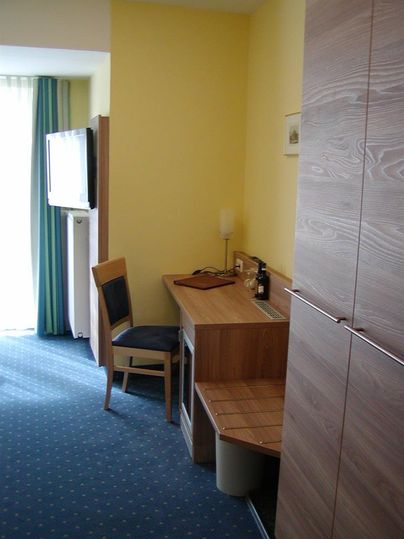 Een eenvoudige kamer met een bureau, een stoel en een televisie. De muren zijn geel en de kamer lijkt licht en vriendelijk.