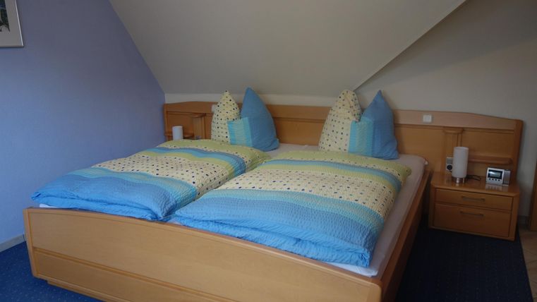 Een gezellige slaapkamer met een tweepersoonsbed en blauw-wit gestreepte dekens. De muren zijn in zachte kleuren gehouden en er zijn nachtkastjes naast het bed.