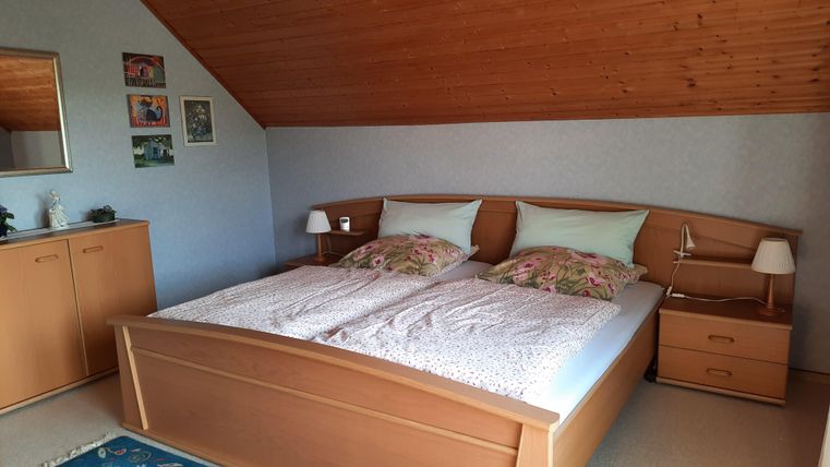 A cozy bedroom with a large double bed. The walls are light, and there is a wooden area with decor and furniture.