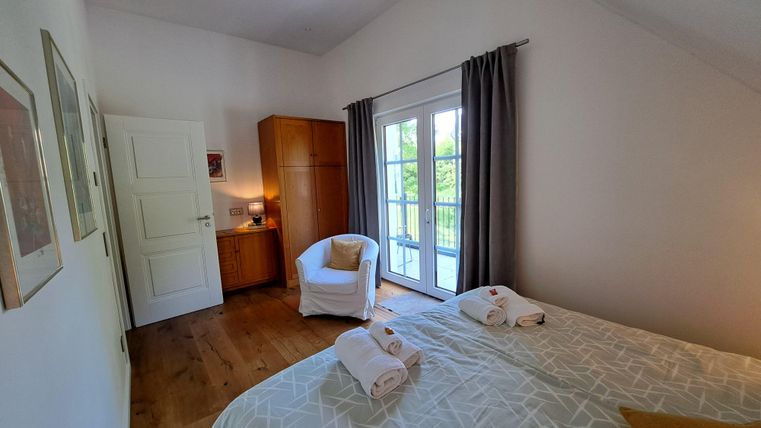 An inviting bedroom with a large window and access to a balcony. The decor is modern and cozy, with bright colors and a comfortable armchair.