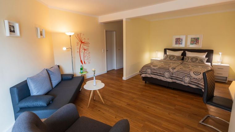 Ein gemütliches Zimmer mit einem großen Bett, einem Sofa und einem kleinen Tisch. Die Wände sind hell gestrichen und es gibt einiges an natürlichem Licht.