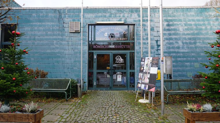 A blue building with a glass entrance door. In front of the building, there are Christmas trees and an information board.