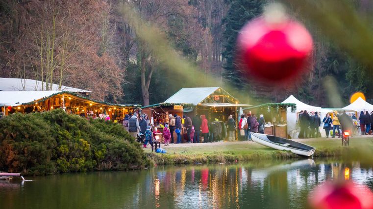 Kerstmarktthema aan de slotgracht van kasteel Satzvey met verschillende kraampjes en veel bezoekers.