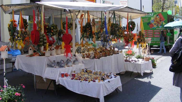 A market stall with various handmade decorations and crafts. There are colorful garlands and small animal figures spread out on tables.