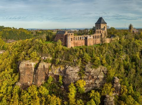 Eine beeindruckende Burgruine auf einem Hügel, umgeben von dichten Wäldern. Der Himmel ist klar und bietet eine malerische Aussicht.