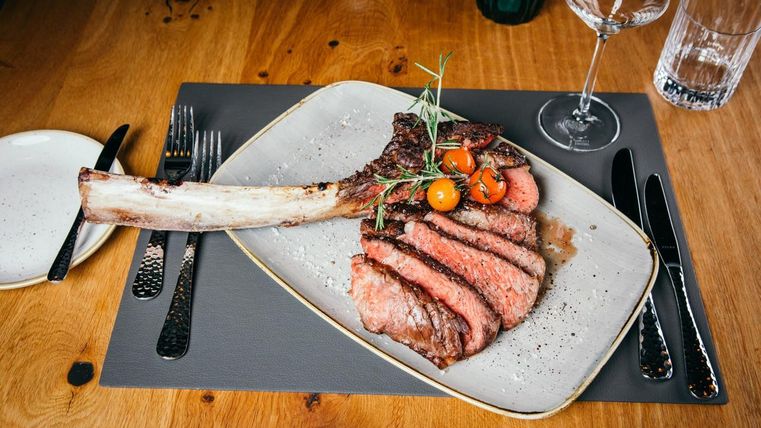 Ein saftiges Steak mit Knochen, schön angerichtet auf einem Teller. Daneben liegen einige Cherrytomaten und eine elegante Tischdekoration.