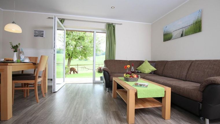 Een lichte woonkamer met een gezellige bank en een tafel. Grote ramen bieden uitzicht op een groene weide.