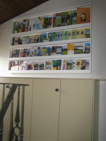Een muur met meerdere planken, versierd met kleurrijke brochures en fotoprints. Daaronder bevindt zich een kast met neutrale deuren.