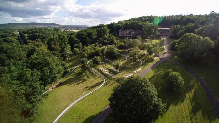 Een schilderachtig landschap met glooiende heuvels en weelderig groen. Op de achtergrond zijn gebouwen en een heldere lucht zichtbaar.