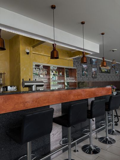 Eine moderne Bar mit eleganten Barhockern und einer gut sortierten Getränkeauswahl. Die Wand ist in warmen Farbtönen gehalten und hat stilvolle Beleuchtung.