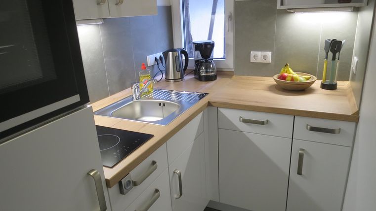 Een moderne keuken met een lichte houten werkblad en witte kasten. Op het werkblad staan fruit en keukenapparatuur.