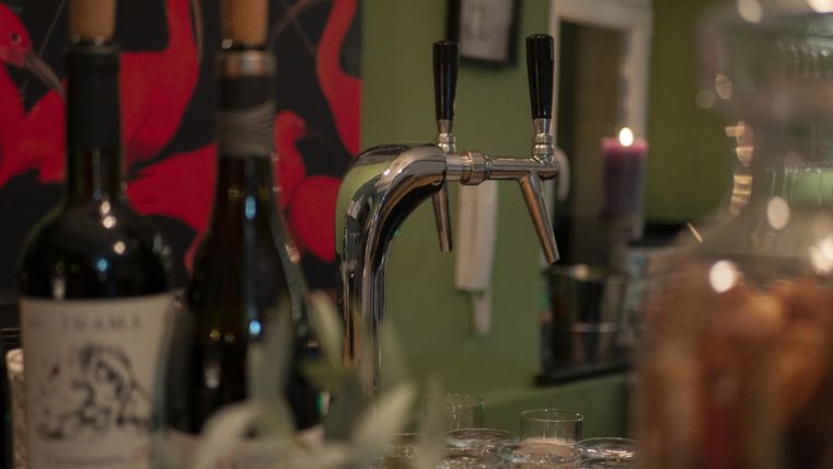 Eine stilvolle Bar mit Weinen und einer Zapfanlage. Im Hintergrund sind rote Flamingos auf einer Wand zu sehen.
