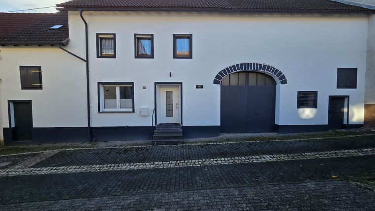 A modern house with a white facade and several windows. The front door is clearly visible and a large gate is also present.